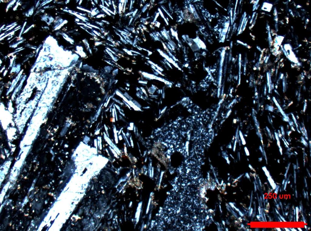 Foto 19: Fenocristales de plagioclasa rodeados por una masa fundamental de plagioclasas más pequeñas, minerales opacos y calcita. Identificación muestra: T3D904 (Foto 20). Coordenadas: 348395/6782019.