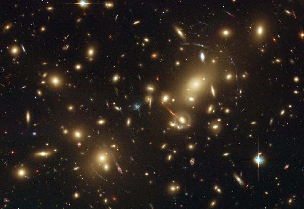 Derecha: cúmulo de galaxias Abell 2218, observado con el Telescopio Espacial Hubble. La mayoría de los objetos de color anaranjado son galaxias perteneciantes al cúmulo.