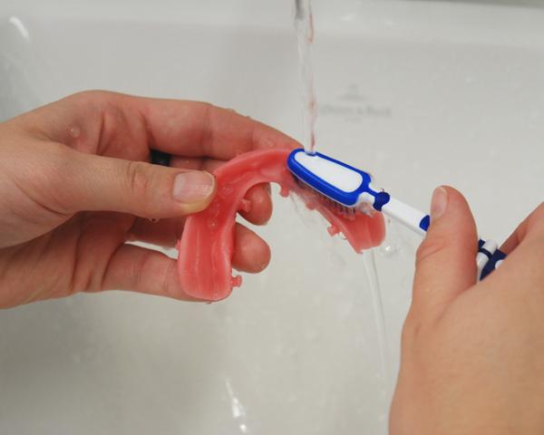 2. Limpieza de la base de la prótesis con un cepillo de dientes blando Cepillar la base de la prótesis con un cepillo de dientes suave y ejerciendo una ligera presión. Img.
