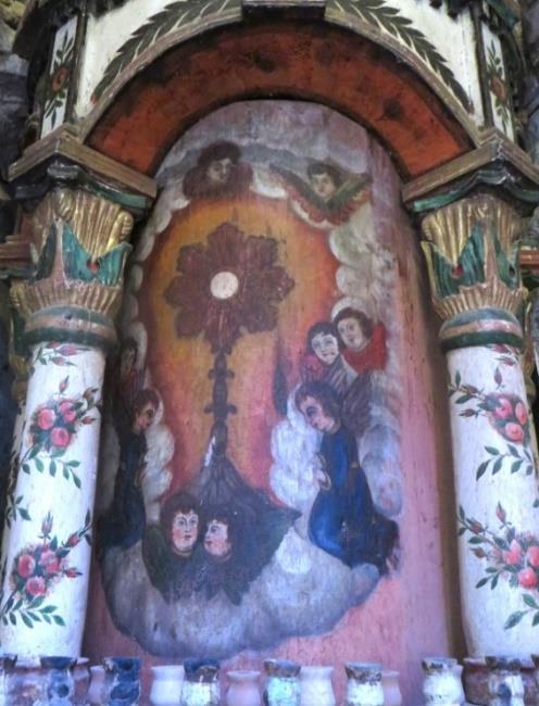 En la parte inferior del altar, se representa en pintura, un círculo con bordes negro, rojo y azul, rodeándole un tres cuartas partes con hojas de olivo, en el interior una cruz de color verde