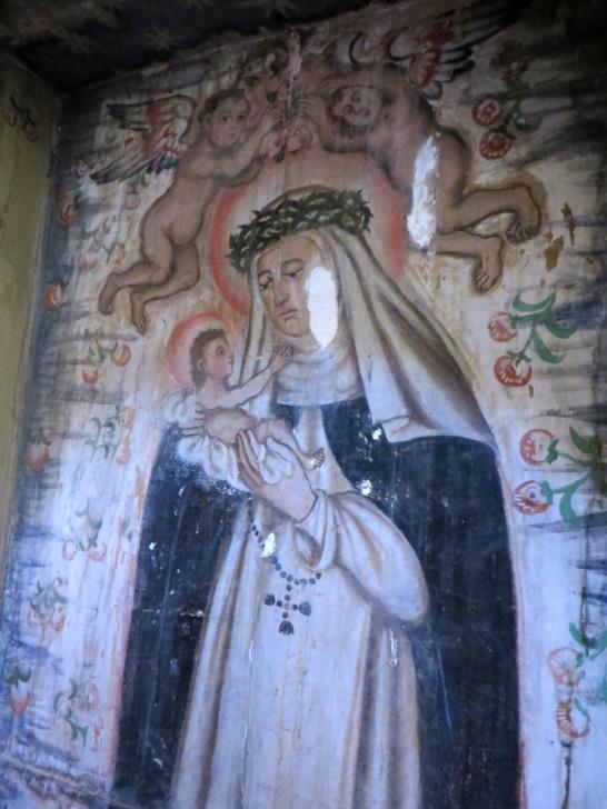 Debajo, en la hornacina central, la imagen pintada de Santa Rosa de Lima sosteniendo al Niño Jesús en sus brazos, y con un rosario.