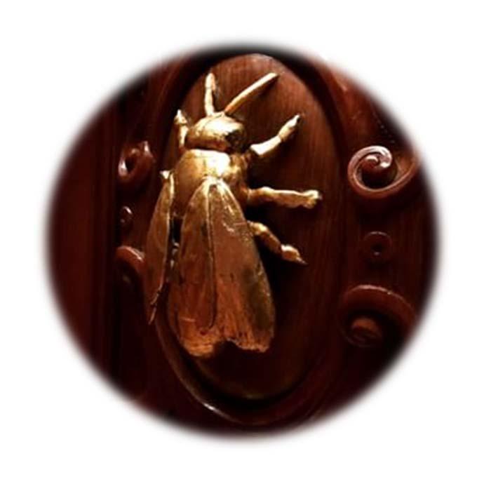 en madera y muestra, en relieve dorado, la figura de una abeja en su centro,