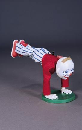 42. Payaso gimnasta. Muñeco que representa a un payaso con chaleco rojo y pantalón blanco a rayas azules.