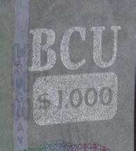 izquierdo la cifra $1000. No aplica a dicha seguridad. CON LUPA 6 Hilo de seguridad Metálico, ancho y holográfico; contiene el escudo de Uruguay, la sigla BCU y 1000 expresado en números.